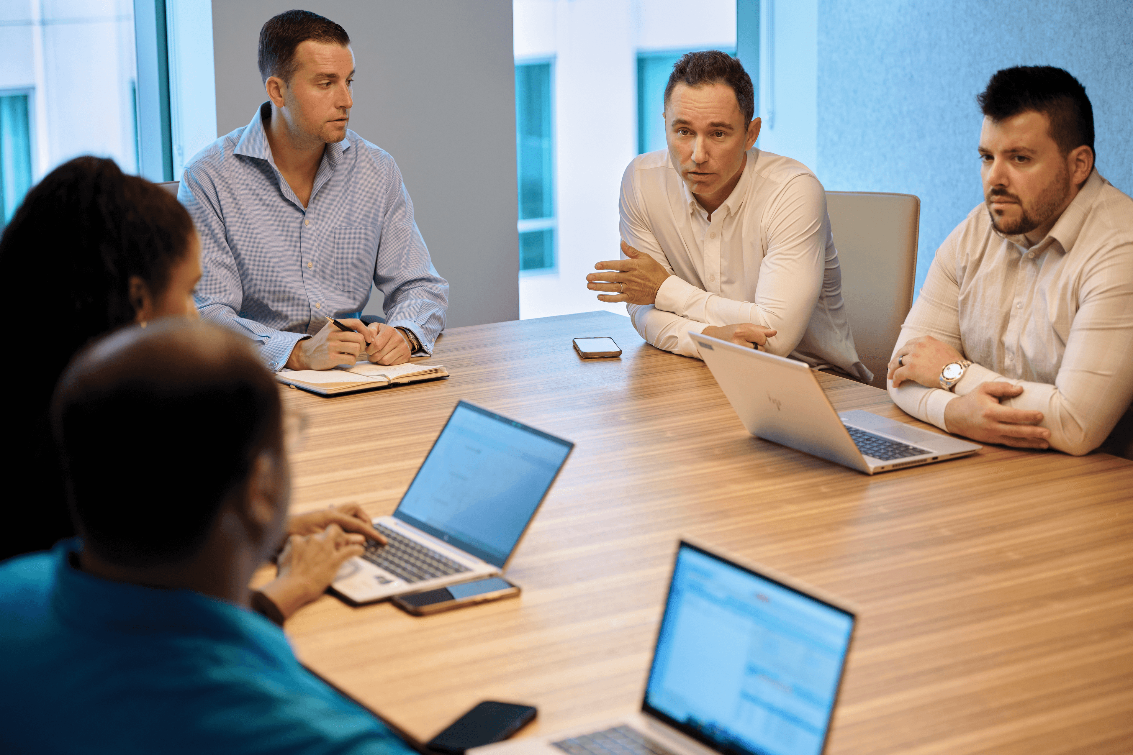 A group of employees gathered around a conference table for a sales meeting with laptops and notepads in front of them