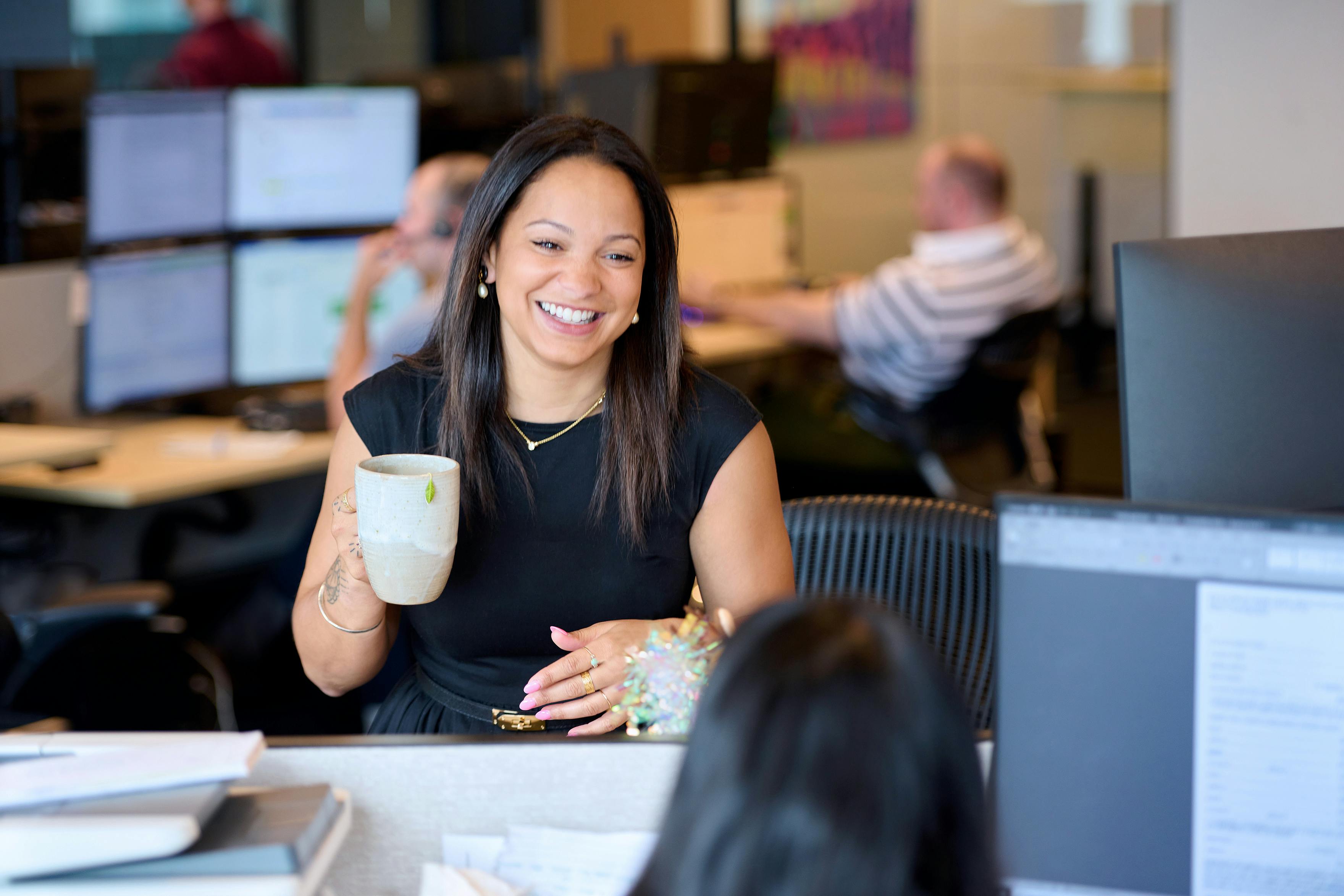 Employee talking to coworker and laughing while holding a coffee mug in the air.